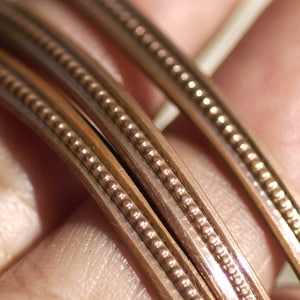 May include: Close-up of three gold-coloured guitar strings with a beaded pattern.