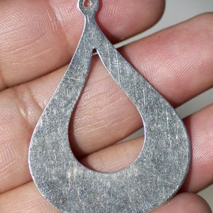 May include: Silver teardrop-shaped earring with a hole at the top for hanging. The earring has a smooth, brushed finish and a cutout in the center.