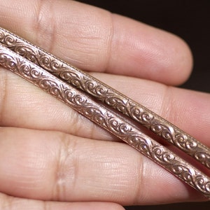 May include: Two silver-toned metal bracelets with an intricate floral design.