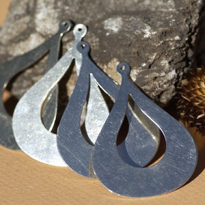 May include: Four silver teardrop-shaped earrings with a cutout design. The earrings are arranged in a row, with the largest earring at the bottom and the smallest earring at the top.