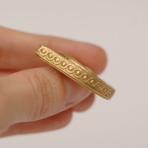 May include: A gold-colored ring with a decorative, beaded pattern around the band.
