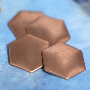 May include: Four hexagonal copper-coloured metal blanks, stacked on a blue surface.