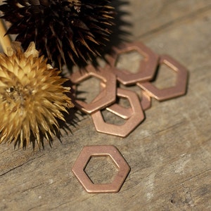 May include: A close-up of a pile of copper-coloured hexagonal metal rings on a wooden surface. The rings are arranged in a random pattern, with some overlapping. The rings are smooth and shiny, and they have a slightly rustic look.