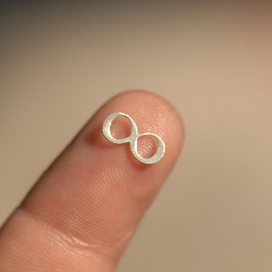 May include: A silver infinity symbol charm, small enough to fit on a fingertip.