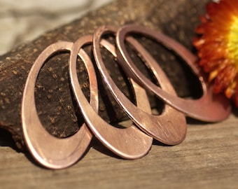 Puede incluir: Cinco aros de cobre de forma ovalada, apilados uno encima del otro, con un acabado liso y pulido. Los aros están sobre una superficie de madera.