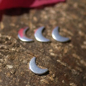 May include: Four silver crescent moon charms on a brown wooden surface.