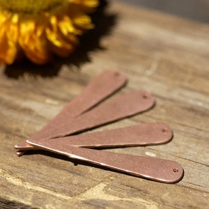 May include: Four copper-colored metal pieces with rounded ends and a hole in each. The pieces are arranged in a fan shape on a wooden surface.