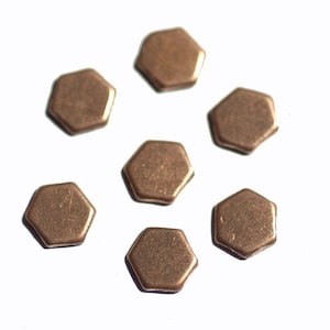 May include: Seven hexagonal copper-coloured metal pieces, scattered on a white surface.
