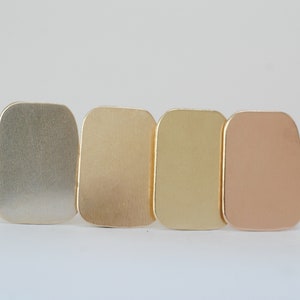 May include: Four rectangular metal samples in different shades of gold, from left to right: silver, light gold, yellow gold, and rose gold.
