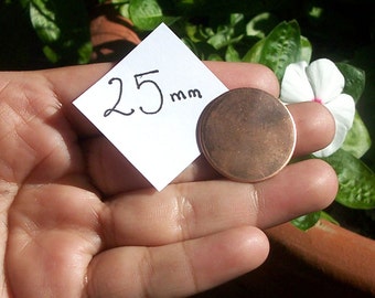 Könnte beinhalten: Eine kupferfarbene Metallscheibe mit einem Durchmesser von 25 mm, die in einer Hand gehalten wird. Die Scheibe ist glatt und glänzend.