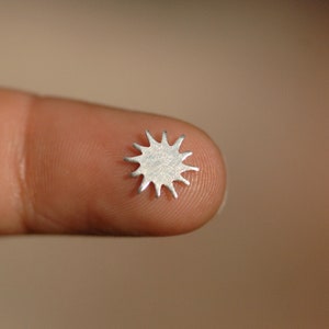 May include: A small, silver, star-shaped metal piece with a textured surface.