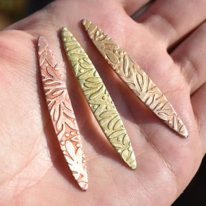 May include: Three long, thin, metal pieces with a decorative, embossed pattern. The pieces are in shades of gold, copper, and bronze.