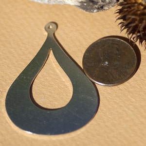 May include: A silver teardrop-shaped pendant with a cutout design. The pendant is about the size of a US penny.