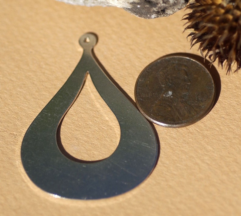 May include: A silver teardrop-shaped pendant with a cutout design. The pendant is about the size of a US penny.