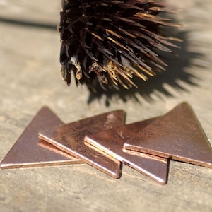 May include: Three copper triangle shapes stacked on top of each other on a wooden surface.