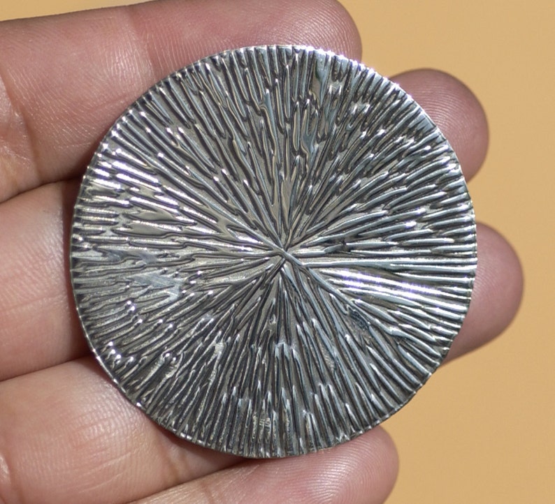 May include: A silver circular pendant with a textured, radial pattern. The pendant has a smooth, polished finish.