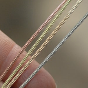 Peut inclure: Trois brins de chaîne, chacun avec une finition métallique différente : argent, or et or rose. Les chaînes sont toutes du même design, avec un petit motif répétitif.