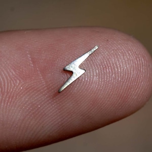 May include: A small, silver lightning bolt charm on a finger.