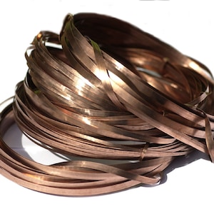 May include: A collection of copper strips, coiled into a bundle. The strips are a warm, metallic brown colour, and appear flat and thin. The image is set against a white background, emphasising the texture and form of the metal.