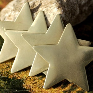 May include: Four gold-colored metal star shapes arranged in a row. The stars are overlapping and have a shiny, metallic finish.