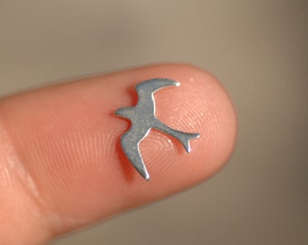 May include: A silver metal bird charm, shown on a finger.
