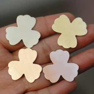 May include: Four metal flower shapes in different colors: silver, gold, rose gold, and brass. The flower shapes are three-dimensional and have a slightly textured surface.