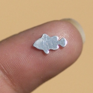 May include: A small, silver, fish-shaped charm. The charm is about the size of a fingernail.