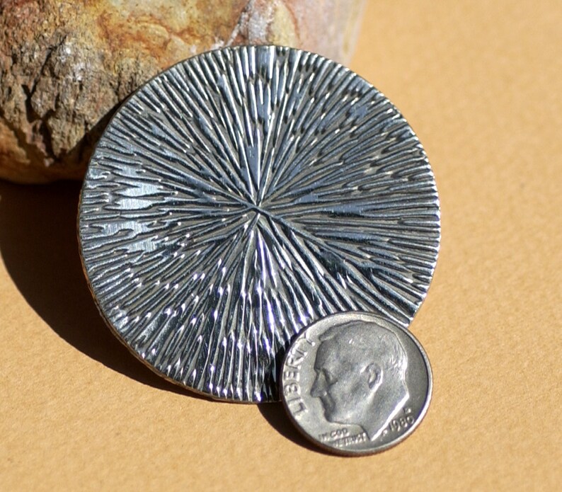 May include: A silver circular pendant with a textured, sunburst design. The pendant is about the size of a dime.