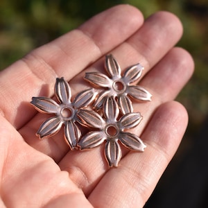 May include: Three rose gold metal flower charms with a hole in the centre. The charms are in the shape of a five-pointed star with rounded edges.
