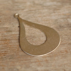 May include: A silver teardrop-shaped pendant with a cut-out design. The pendant has a hole at the top for attaching a chain or cord.