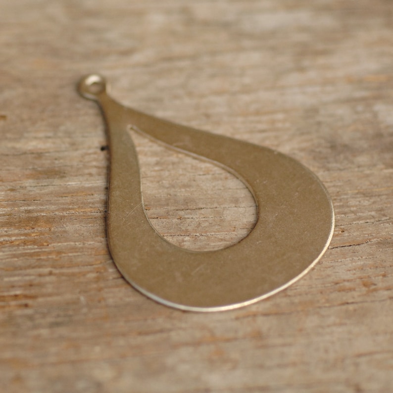 May include: A silver teardrop-shaped pendant with a cut-out design. The pendant has a hole at the top for attaching a chain or cord.