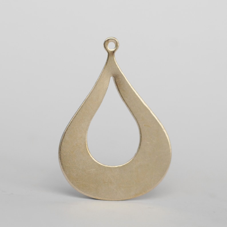 May include: A gold-toned metal pendant shaped like a teardrop with a cutout in the center. The pendant has a loop at the top for attaching to a chain or cord.