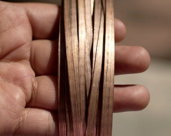 May include: A close-up of a bundle of thin, flat copper strips, held in a hand. The strips are arranged in a staggered pattern, creating a textured surface.