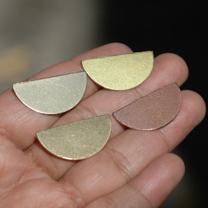 May include: Four half-circle metal shapes in different colors. The shapes are gold, brass, and copper. The shapes are arranged in a row on a hand.