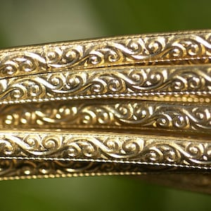 Könnte beinhalten: Nahaufnahme einer goldfarbenen Metallverkleidung mit einem dekorativen, wirbelnden Muster.