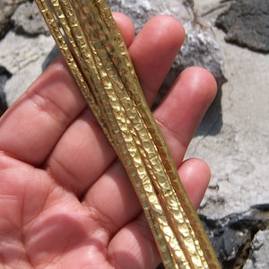 Può includere: Primo piano di un fascio di cinque aste metalliche dorate con una texture martellata.