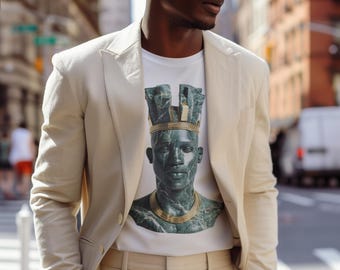 Può includere: Un uomo indossa un completo color crema con una maglietta bianca con una grafica verde e oro di un busto. Il completo comprende una giacca e pantaloni abbinati. Lo sfondo mostra una strada cittadina con edifici.