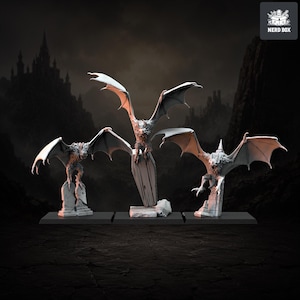 Pode incluir: Três figuras em miniatura cinzentas sem pintura de criaturas aladas com garras afiadas e orelhas pontiagudas. Cada criatura está pousada numa base diferente: uma lápide, um caixão e um pilar de pedra partido. O texto NERD BOX é visível.