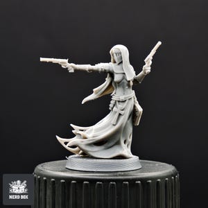 May include: A gray miniature figurine of a robed figure holding two pistols. The figure wears a veil and a cross is visible on the front of the robe. The figurine is on a black base. The Nerd Box logo is in the lower left corner.