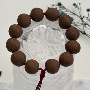 May include: A brown wooden beaded bracelet with a red string closure. The beads are round and have a smooth, matte finish.