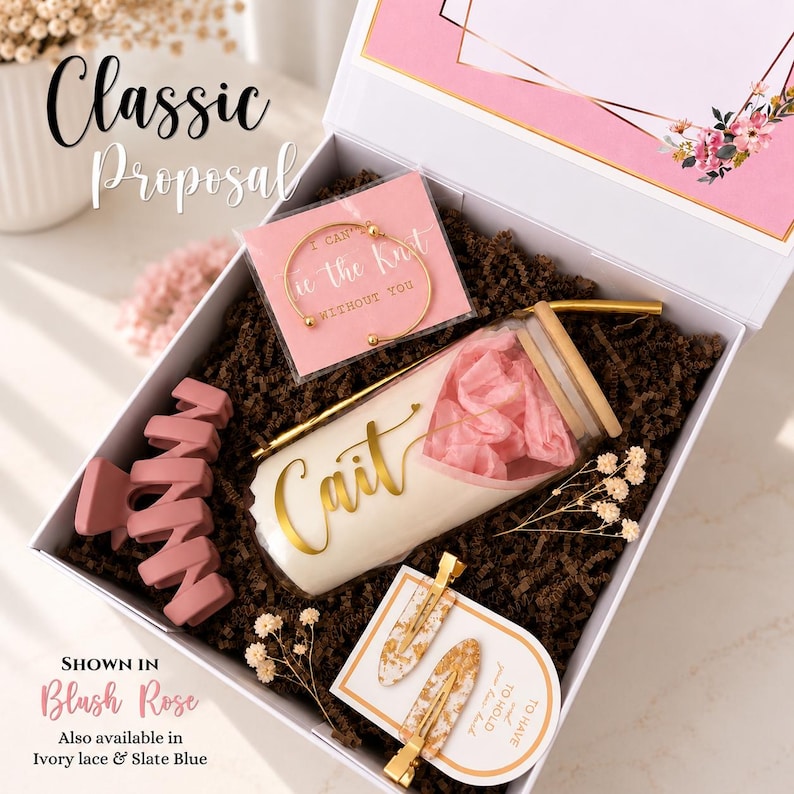 May include: A white gift box containing a glass tumbler with a bamboo lid, a gold-tone bangle, a matte pink hair claw, and two gold-flecked hair clips. The tumbler features the name Cait in gold script. The box includes floral-themed cards.