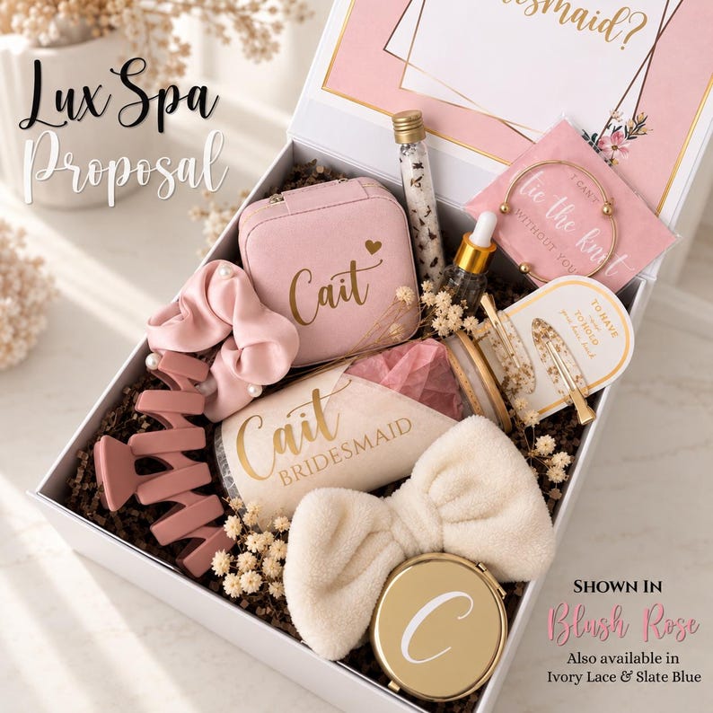 May include: A white gift box containing a pink jewelry case labeled Cait, a pink scrunchie, a pink hair claw, a glass vial of bath salts, a gold bangle, a hair clip, a tumbler labeled Cait Bridesmaid, a white headband, and a gold compact mirror.