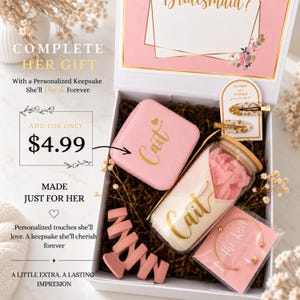 May include: A white gift box containing a pink square jewelry case with the name Cait, a glass tumbler with a bamboo lid and the name Cait, a pink hair claw clip, two gold-flecked hair clips on a card, and a gold bracelet on a card.