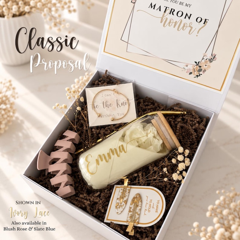 May include: A white gift box containing a glass tumbler with a bamboo lid and the name Emma, a gold-toned bracelet on a card reading I can't tie the knot without you, two hair clips with gold flakes, and a matte mauve hair claw on brown paper filler.