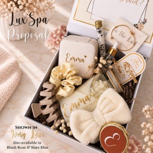 May include: A gift box containing a personalized jewelry case with the name Emma, a cream scrunchie with pearls, a beige hair claw, a glass vial of bath salts, a dropper bottle, a gold bangle, hair clips, a plush bow headband, and a compact mirror.