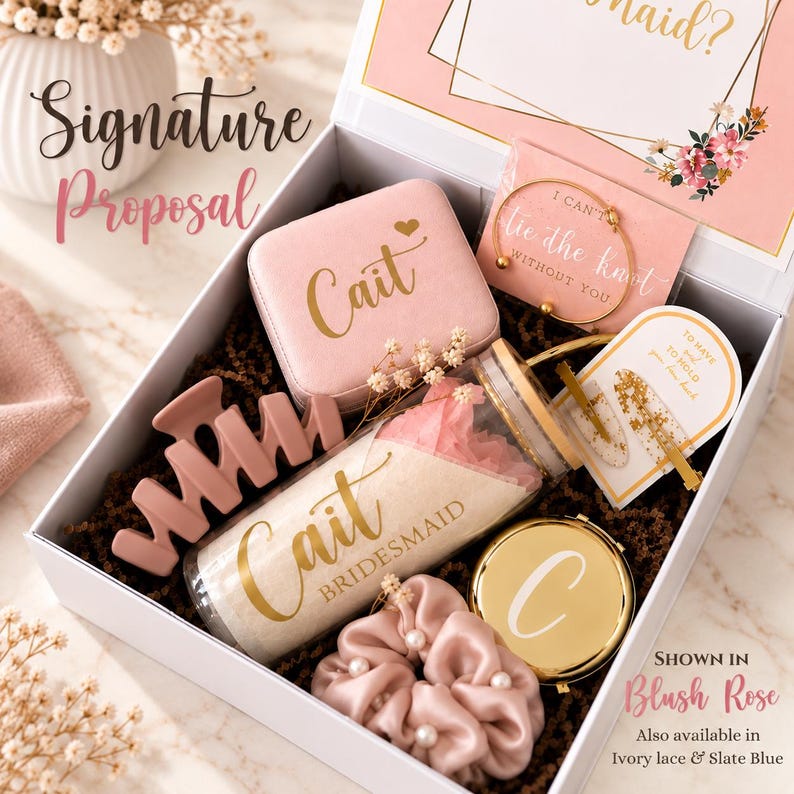May include: A white gift box containing a pink velvet jewelry case with the name Cait, a gold bangle with the text I can't tie the knot without you, a pink hair claw, a clear tumbler with the name Cait, a gold compact mirror with the letter C, and a pink scrunchie.
