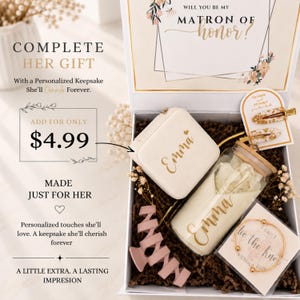 May include: A gift box containing a white jewelry case with the name Emma, a glass tumbler with a bamboo lid and the name Emma, two gold-flecked hair clips, a pink hair claw, and a gold-toned bracelet on a card reading I can't tie the knot without you.