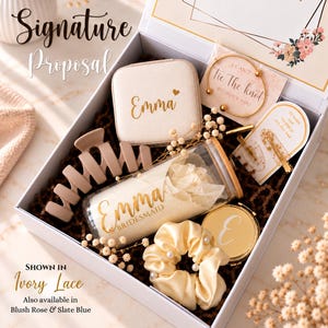 May include: A white gift box containing a beige jewelry case with the name Emma, a glass tumbler with a bamboo lid labeled Emma Bridesmaid, a matte beige hair claw, a cream satin scrunchie with pearls, a gold compact mirror, and a gold bangle.