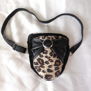 May include: A black and brown leopard print pouch with a black bow and a silver button. The pouch has a black adjustable strap.