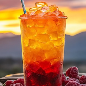 May include: A tall glass filled with a layered drink, transitioning from deep red at the bottom to orange at the top, topped with ice cubes. A blue and white striped straw is in the drink. Fresh raspberries are scattered around the glass.